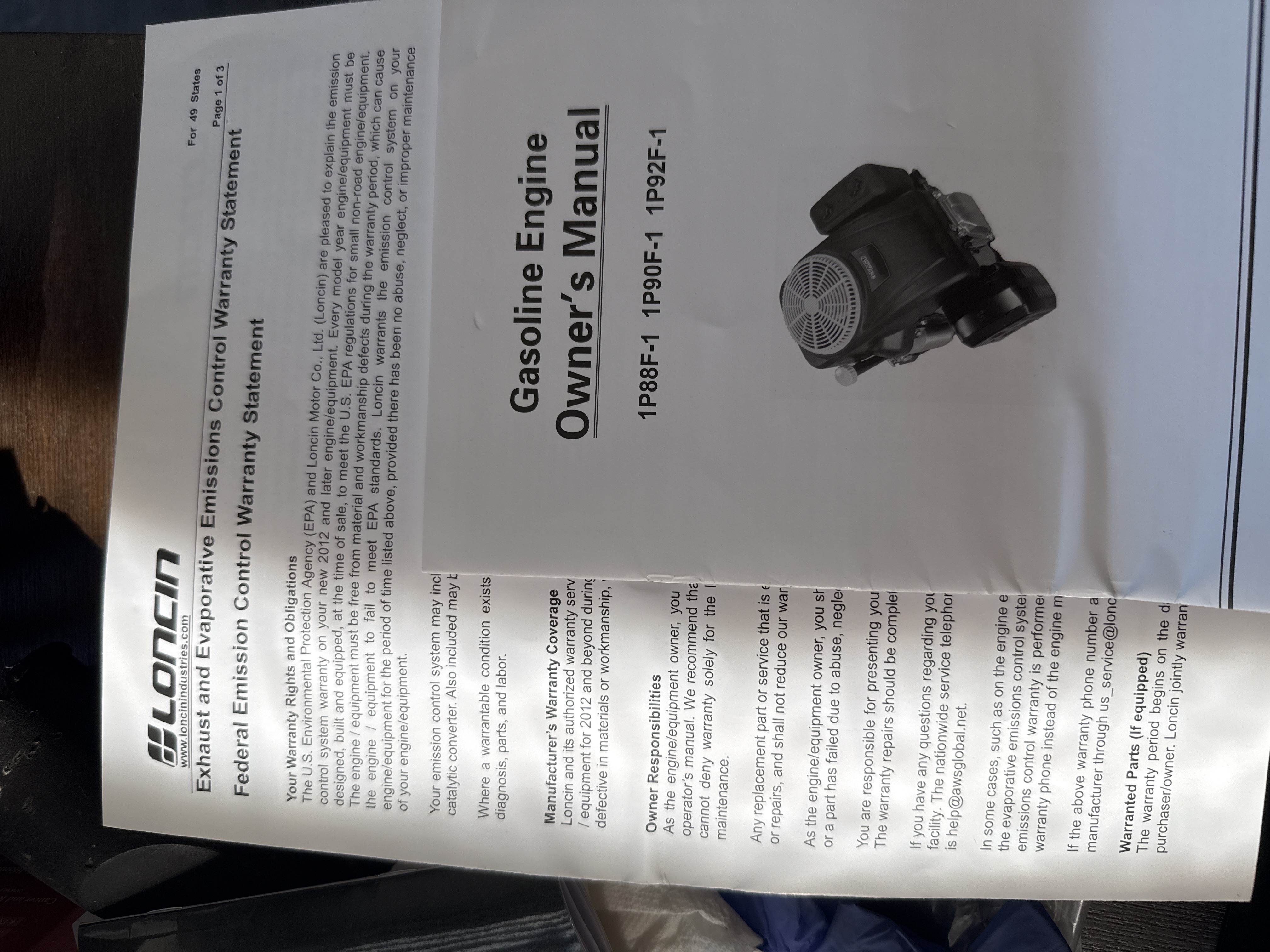 Photograph of the Loncin gasoline engine owner's manual and emissions warranty papers that accompanied the mower.